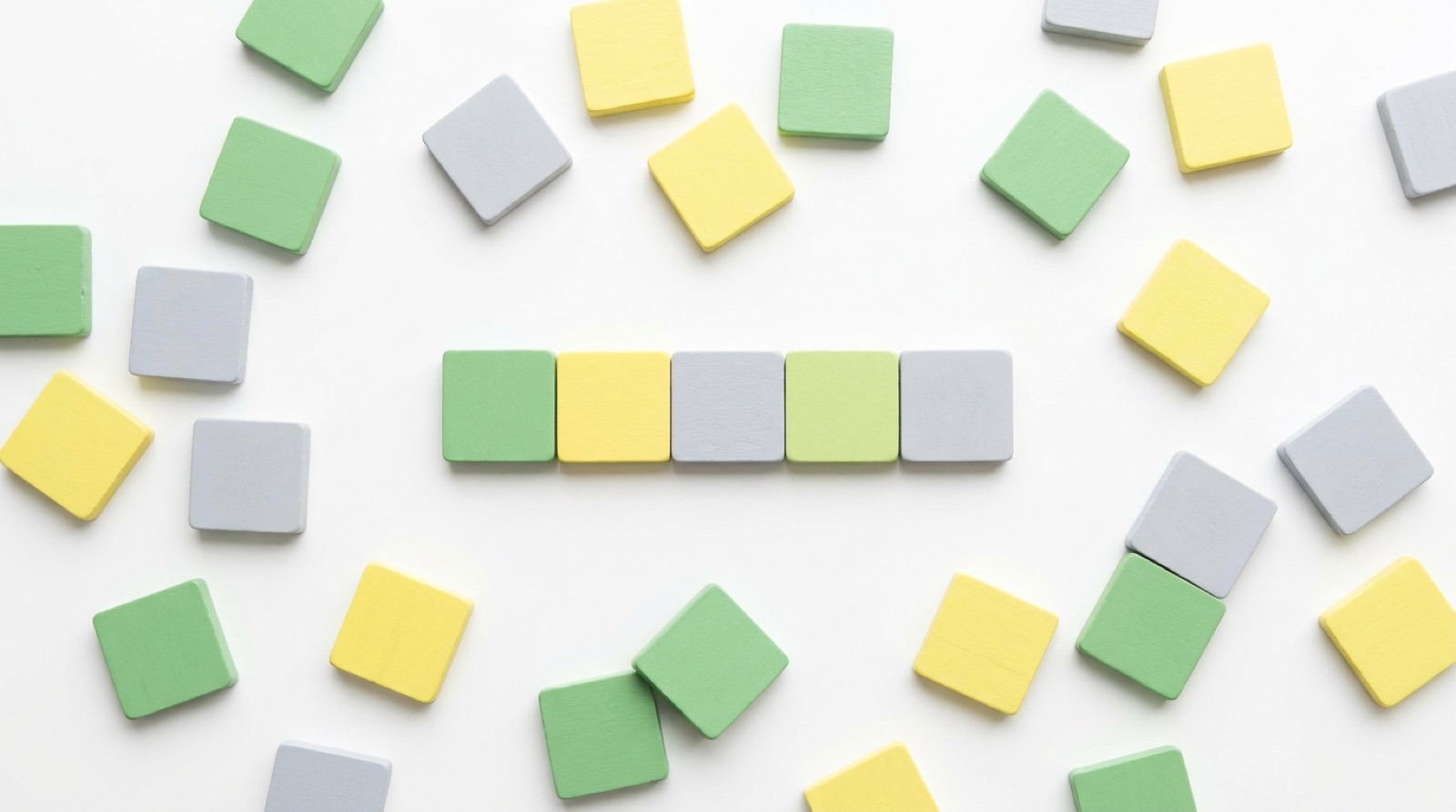 Letter tile cards in green, gold and gray spread across a white table